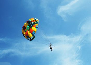 Low angle view of man parasailing against blue sky