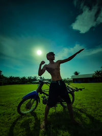 Man with arms raised on field against sky