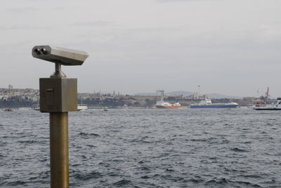 Coin-operated binoculars by sea against sky