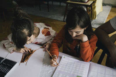 Girl doing homework while sister drawing at table