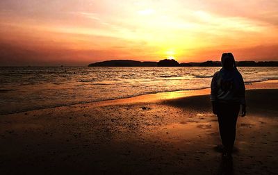 Rear view of woman standing on beach during sunset