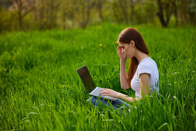 Young woman using mobile phone while sitting on grassy field