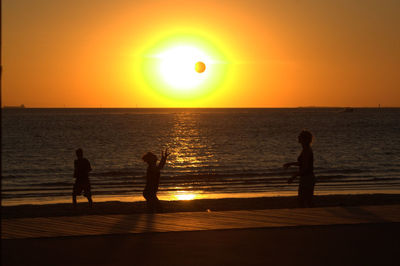 Silhouette people on beach at sunset