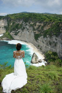 Rear view of woman standing on rock by sea