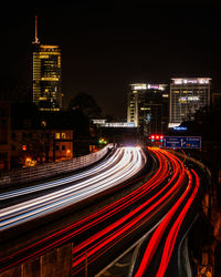 Light trails on road against illuminated buildings in city at night