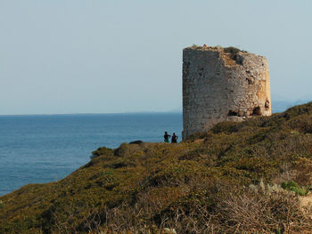 Scenic view of old structure on cliff by sea against clear sky