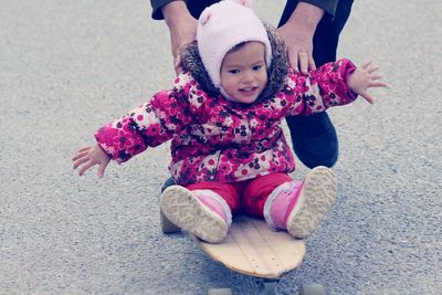 Low section of woman pushing daughter sitting on skateboard