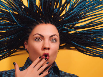 Close-up portrait of young woman with braided hair against yellow background