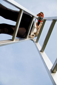 Directly below shot of young woman using smart phone while standing on ladder against clear sky