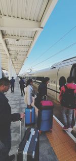 People standing on railroad station platform against clear sky