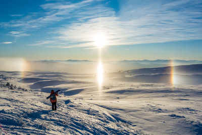 Woman standing on snow covered landscape against sky during sunset