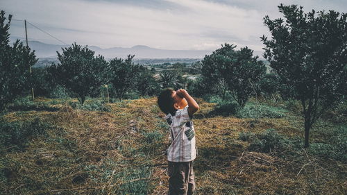 Rear view of woman standing on field against sky