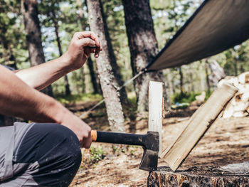 Midsection of man cutting wood in forest