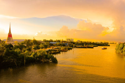 Scenic view of river by buildings against sky during sunset