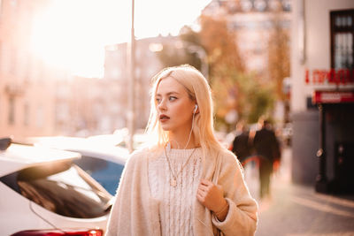 Young woman listening music on earphones while walking on city street