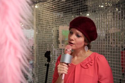 Young woman singing while holding microphone against net