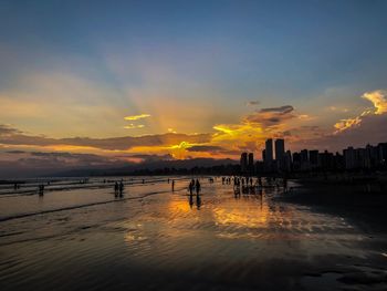 People at beach against sky during sunset