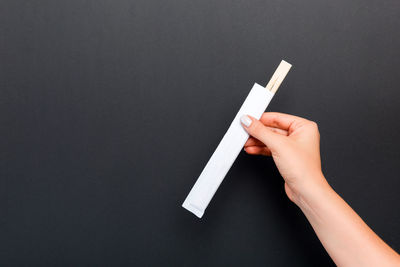 Close-up of hand holding chopsticks against colored background