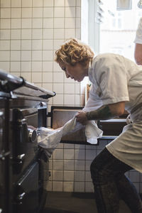 Side view of female chef using oven in restaurant kitchen