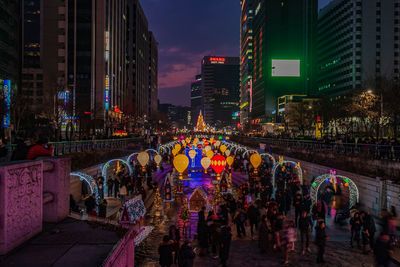 People on illuminated street amidst buildings in city at night