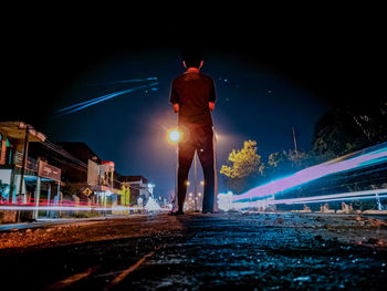 Rear view of man standing on road at night