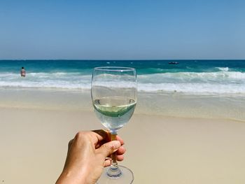 Midsection of man holding glass at beach against sky