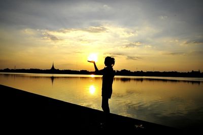 Silhouette man standing by lake against sky during sunset