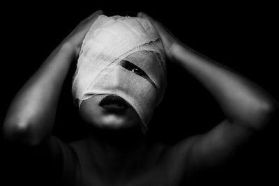 Close-up portrait of young woman face wrapped in bandage against black background