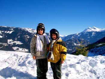 Portrait of couple standing on snow covered mountain against clear blue sky