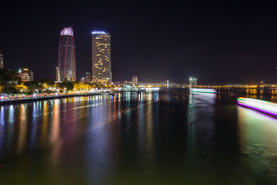 Illuminated buildings by river against sky at night