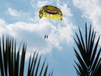 Low angle view of people parasailing against sky