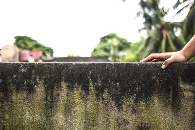 Cropped hand on concrete wall against clear sky