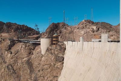 Wall of hoover dam by rock formations and electricity pylons against clear blue sky