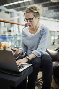 Businesswoman using laptop and smart phone at airport lobby