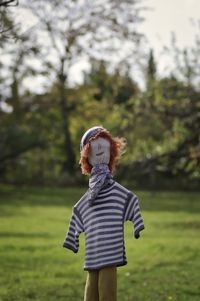 Cropped fingers with small scarecrow toy against trees