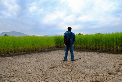 Rear view of man standing on field against sky