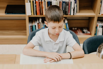 Schoolboy sitting on table and reading book in library at school. preparing for homework. 