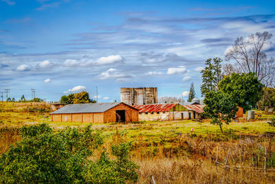 Houses on field by trees against sky