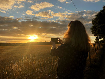 Woman photographing on field during sunset