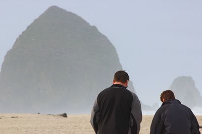 Rear view of men standing on beach against sky