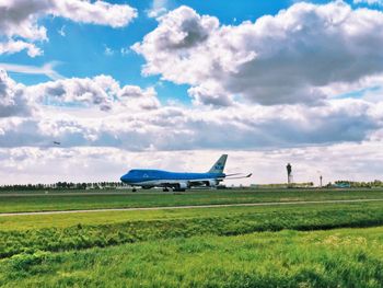 Airplane flying over grassy field against sky