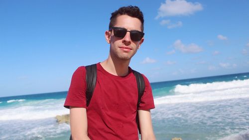 Portrait of young man standing at beach against sky