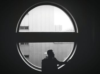 High angle view of man standing against circular glass window in darkroom