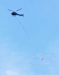 Low angle view of helicopter carrying play equipment in blue sky