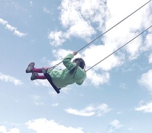 Low angle view of girl swinging on swing against cloudy sky