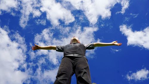 Low angle view of man standing with arms outstretched against blue sky