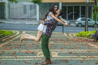 Man lifting girlfriend on footpath in city