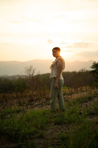 Full length of boy standing on field against sky during sunset