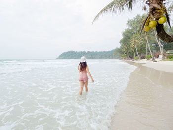 Hipster young woman in bikini walking barefoot on the beach and look to the little waves. 