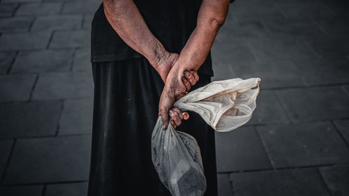 Midsection of woman holding plastic while standing on footpath